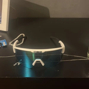 solglasögon från Bliz - Säljer ett par coola sportglasögon från Bliz i vitt och svart med blå spegelglas. Perfekta för träning eller en solig dag. De har en modern design och sitter bekvämt på huvudet. Passar både för cykling och löpning. Använda men i mycket bra skick!