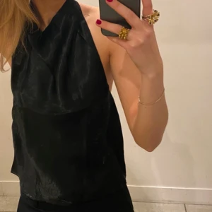 Svart halterneck topp - Snygg svart halterneck topp i ett glansigt material. Perfekt för en utekväll eller fest. 