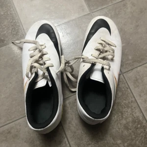 Nike  fotbollsskor  - Hej! Jag säljer ett par vita Nike fotbollsskor med svarta och orange detaljer. Skorna är i mycket bra skick och jag säljer dem för att dem inte passar mig. 