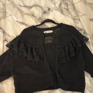 Svart kofta från Zara - Säljer en svart kofta från Zara i storlek M men skulle säga att det passar en som bär xs/s också . Den har vackra spetsdetaljer och volanger längs axlarna. Perfekt för höst och vår, med knappar framtill för enkel stängning. Passar både till vardags och festliga tillfällen.