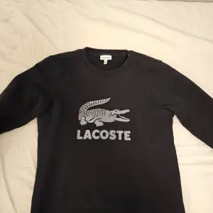 Säljer en svart sweatshirt från Lacoste i mycket bra skick. Den har en stor krokodil-logga på framsidan och är perfekt för både vardag och chill. Tröjan har långa ärmar och är superbekväm. Perfekt för höst och vinter! Originalpris är 1000 kr. Tar endast swish.