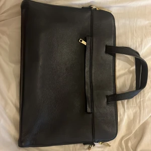 Svart datorväska i skinn - Säljer en stilren svart datorväska från Wera i skinn med guldiga detaljer och dragkedja. Väskan har ett rymligt fack utpå och två fack innuti. Perfekt för o ha till datorn i skolan och jobbet. Den har två handtag för enkel bärning. Använd en del men fortfarande i bra skick!💞