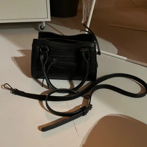 Svart handväska med axelrem - Snygg svart handväska i skinn med avtagbar axelrem. 