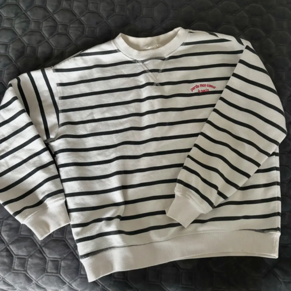 Säljer en superfin vit och svart randig sweatshirt med texten 'perdu mon coeur à paris' broderad i rött på bröstet. Tröjan har en klassisk rund hals och långa ärmar, perfekt för en avslappnad stil. Den är i mycket bra skick och passar perfekt till både jeans och kjol. Perfekt för höst och vår!. Neuletakit & Villapaidat.