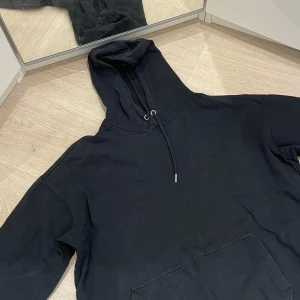 Svart hoodie (luvtröja) - Säljer en klassisk svart hoodie i mycket bra skick. Den har en stor ficka fram och justerbar huva med snören. Perfekt för både mysiga hemmakvällar och vardagsbruk. Passar till allt och är superbekväm!