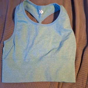 Blå sporttopp från Hummel - Säljer en blå sporttopp från Hummel i mycket bra skick. Den är ärmlös med en ribbad kant och har en snygg brottarrygg för extra stöd under träningen. Perfekt för gymmet eller löprundan!