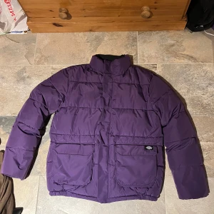 Lila pufferjacka från Dickies - Säljer en snygg lila pufferjacka från Dickies i storlek small men sitter som M. Jackan är perfekt för kalla dagar med sin tjocka vaddering och har praktiska fickor framtill. Den är i mycket bra skick och redo för vinterns äventyr! 💜