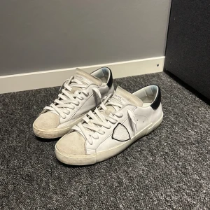 Philippe Model skor - Snygga vita sneakers från Philippe Model i bra skick. De har en stilren design med svarta detaljer på hälen och en diskret logga på sidan. Skorna har snörning och en bekväm passform, perfekta för vardagsbruk. De är i stl 42. Skicket är bra. Kvttio och sånt finns! (Köpta på Philippe models egens hemsida)