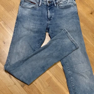 Blå jeans från Tommy Hilfiger - Säljer ett par snygga blå jeans från Tommy Hilfiger i modellen Scanton. De har en klassisk femficksdesign med knappgylf och är i bra skick. Med slim fit passform är de Perfekta för både vardag och fest! Strl w30 L 34