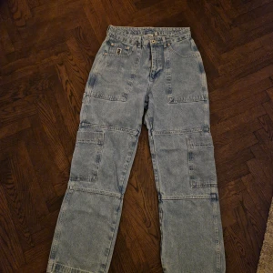 Blå cargopants från Ragged Jeans - Säljer ett par blå cargopants från Ragged Jeans i bra skick. De har en loose passform med flera praktiska fickor och är perfekta för en avslappnad stil. Tillverkade i jeansmaterial, vilket gör dem både slitstarka och bekväma. Perfekta för höst och vår!
