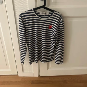 Randig långärmad tröja från Comme des Garçons - Säljer en snygg randig tröja från Comme des Garçons i blått och vitt. Den har ett coolt rött hjärta på bröstet och är perfekt för både vardag och fest. Tröjan är i mycket bra skick och gjord av mjukt bomullsmaterial. Passar perfekt till jeans eller kjol! Ny pris 1000kr mitt pris 399kr