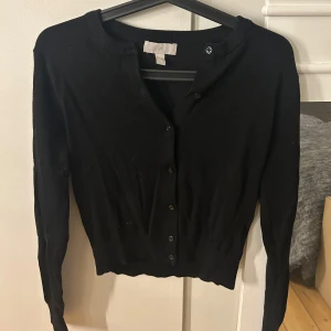 Svart kofta med knappar - Säljer en svart kofta i mycket bra skick. Den har långa ärmar och är tightare nedtill. Oanvänd.
