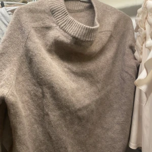 Beige stickad tröja - Mysig beige stickad tröja med ribbad krage och långa ärmar. Perfekt för kyliga höst- och vinterdagar. Tröjan har en enkel och stilren design som passar till det mesta. Ett måste i garderoben för den som älskar komfort och stil. Lite nopprig på armen men det går säkert att få bort!