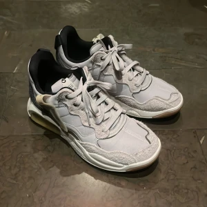 Jordan ma2 skor - Säljer ett par grå sneakers i mycket bra skick. De har en snygg design med snörning och en bekväm sula. Perfekta för vardagsbruk eller träning. Skorna har en cool detalj med en gul accent på hälen som ger dem en unik look. Använt en gång och är i perfekt skick. Säljs p.g.a att de inte används 