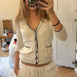Vit kofta med svarta detaljer - Säljer en superfin vit kofta med svarta knappar och kantdetaljer. Den har trekvartsärmar och en v-ringad design som ger en stilren look. Perfekt för både vardag och fest! 🖤