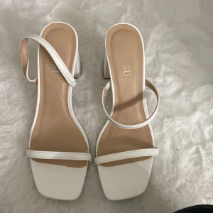 Vita sandaler med klack - Snygga vita sandaler med klack och smala remmar. Perfekta för  fester eller en dag på stan. De har en fyrkantig tå och en bekväm passform. Stilrena och enkla att matcha med olika outfits.