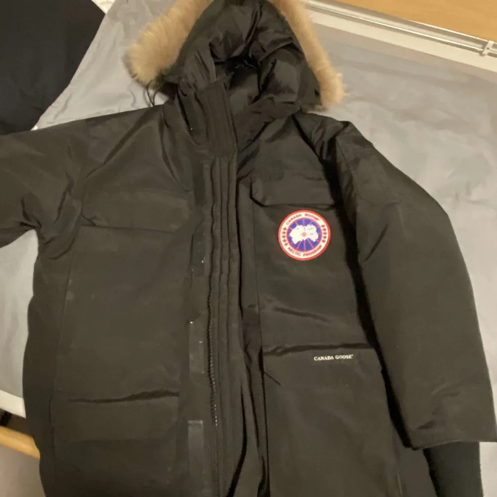 Säljer en svart Canada Goose dunjacka i mycket bra skick. Jackan har en pälsfodrad huva och är perfekt för kalla vinterdagar. Den har en dragkedja framtill och är långärmad. Märkets logga syns tydligt på bröstet. Perfekt för dig som vill hålla värmen med stil!. Jackor.