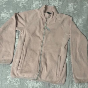 Ljusrosa fleecejacka från Plink - Mysig ljusrosa fleecejacka från lager i bra skick. Perfekt för kyliga dagar med dragkedja framtill och praktiska fickor. Jackan har en normal passform och är långärmad, vilket gör den idealisk för höst och vår. Superbekväm och lätt att matcha med andra plagg! PRISET GÅR ATT DISKUTERA 