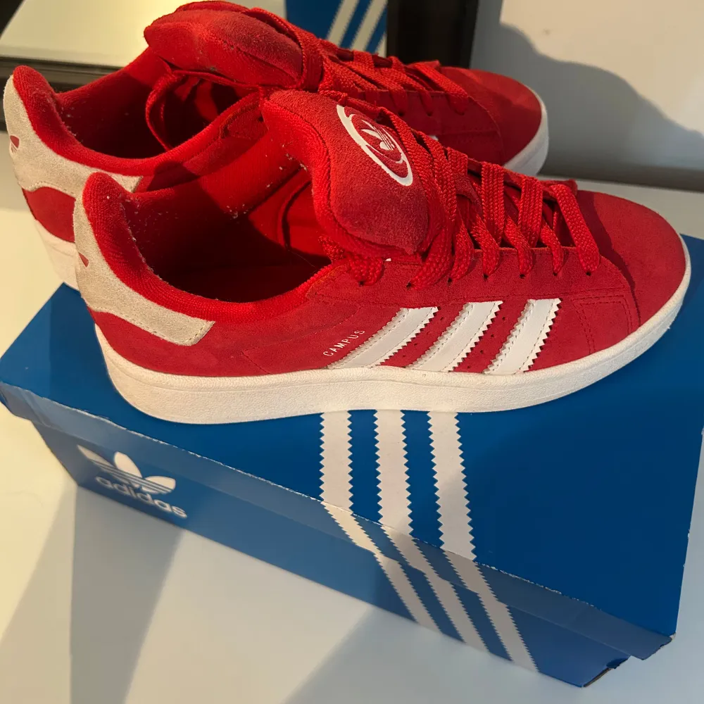 Säljer ett par snygga röda Adidas sneakers i mycket bra skick. De har en klassisk design med vita detaljer och snörning. Perfekta för både vardag och fest! Storleken är normal och de är gjorda i syntetmaterial. Nästan nya använd två gånger.. Skor.