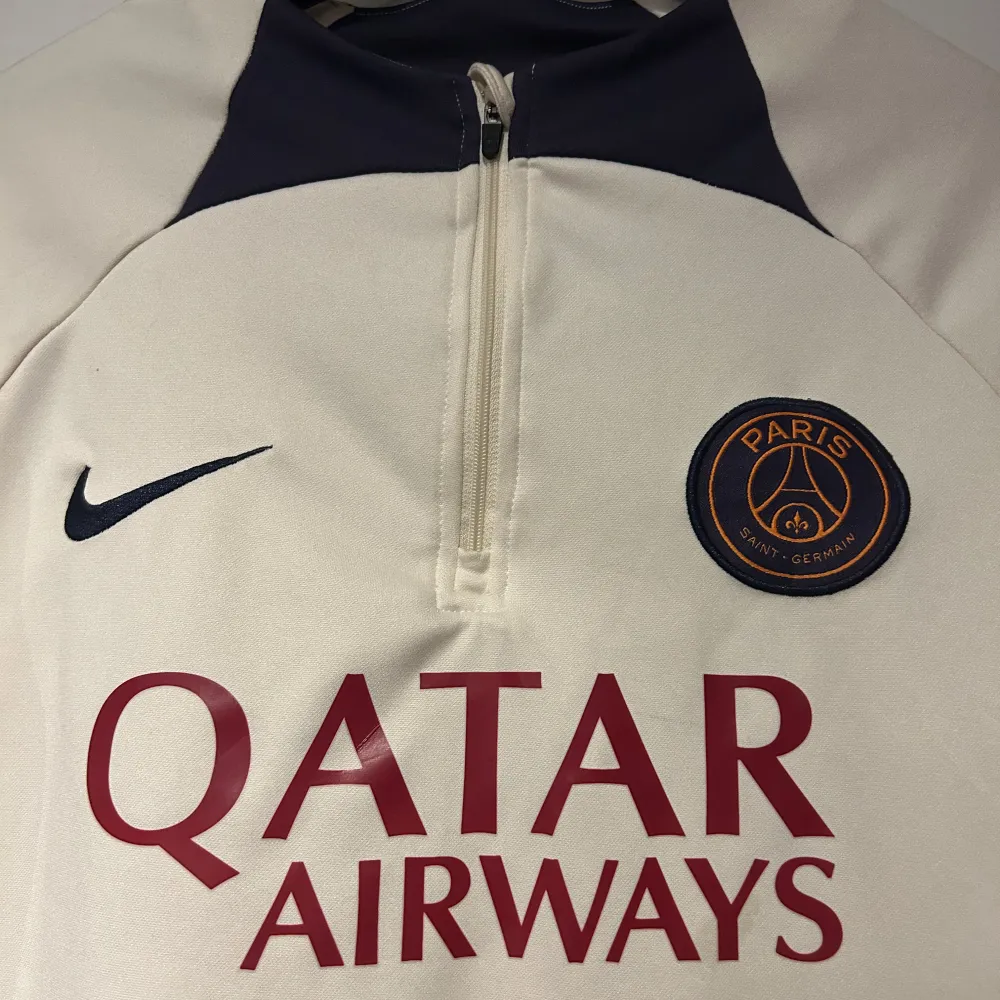 Säljer en snygg vit långärmad fotbollströja från Nike med Paris Saint-Germain-logga och Qatar Airways-tryck. Tröjan har en dragkedja vid halsen och mörkblå detaljer. Perfekt för fotbollsfans som vill ha något stilrent och bekvämt att bära. Hör av er vid minsta fundering 🍾. Tröjor & Koftor.