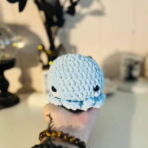 Ljusblå stickad bläckfiskleksak - En supergullig ljusblå stickad bläckfiskleksak med stora svarta ögon. Den är mjuk och perfekt som en söt dekoration eller en mysig kompis att krama. Perfekt för alla som älskar unika och handgjorda leksaker!