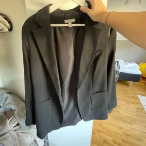 Svart kavaj - Säljer en stilren svart kavaj med klassisk design. Den har en enkel knapp framtill och två fickor. Perfekt för både vardag och festliga tillfällen. Passar bra till höst och vår.