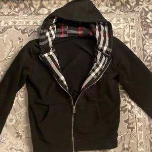 Burberry Zip - Svart burberry zip hoodie i storlek M, den är för liten för mig därför säljer jag. Använd några gånger men inte alls för mycket så fortfarande i väldigt bra skick. Passar nog runt 175 cm.