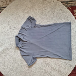 Grå slim fit topp från Smog - Säljer en stilren grå slim fit topp från Smog. Den har en dragkedja framtill och korta ärmar, perfekt för en avslappnad men ändå snygg look. Materialet känns mjukt och bekvämt, och den grå färgen gör den lätt att matcha med andra plagg.