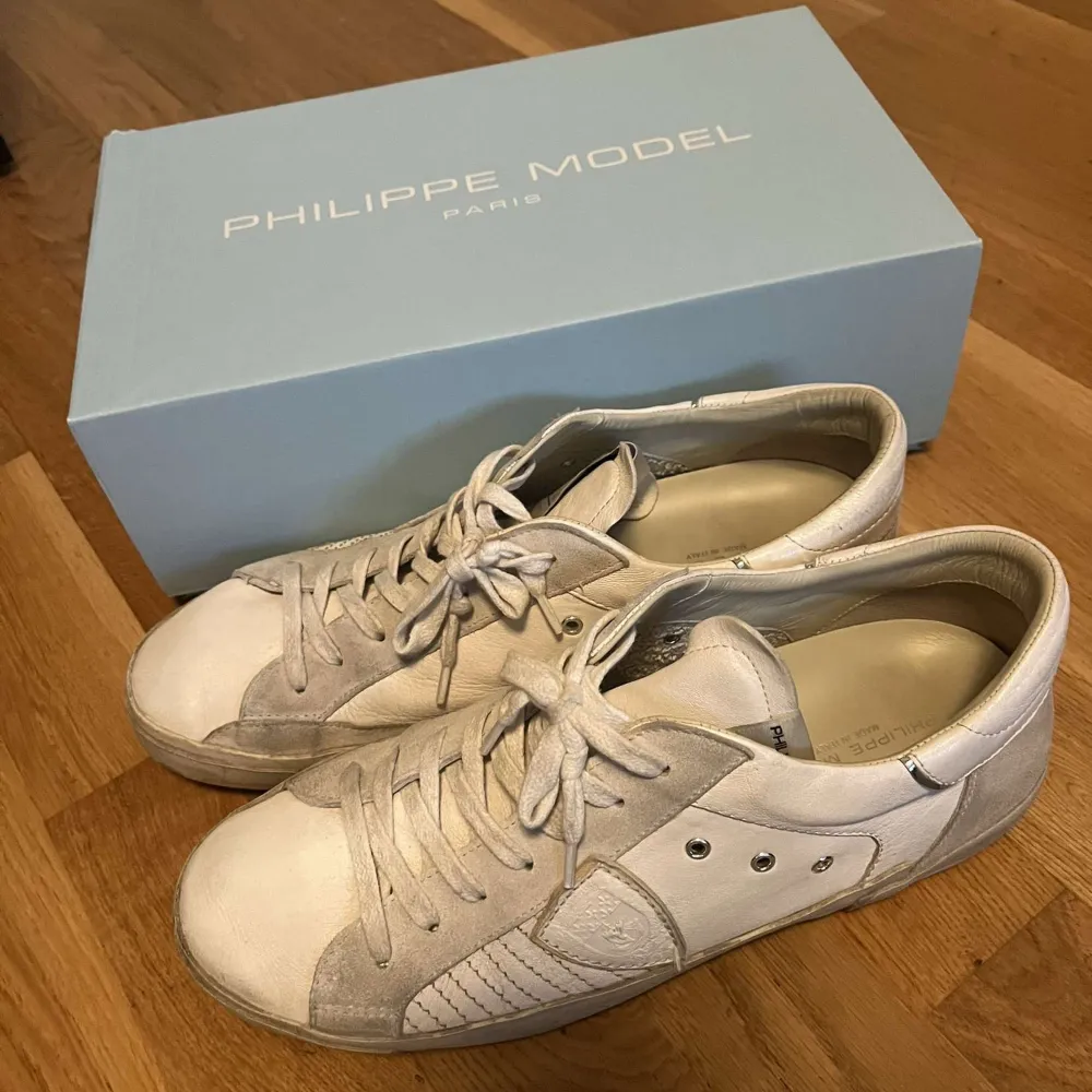 Säljer ett par snygga vita sneakers från Philippe Model. Skorna har en stilren design med snörning och detaljer i mocka. De är i bra skick och perfekta för både vardag och fest. Kommer med originalkartong.. Skor.