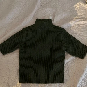 Mörkgrön ribbad polotröja - Säljer en snygg mörkgrön ribbad polotröja. Perfekt för höst och vinter med sin mysiga och varma känsla. Tröjan har trekvartsärmar och en hög krage som håller dig varm. Passar både till vardags och lite finare tillfällen.