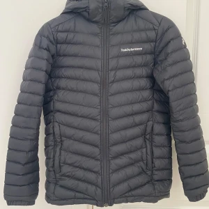 Svart dunjacka från Peak Performance - Säljer en svart dunjacka från Peak Performance. Jackan har en dragkedja framtill och är långärmad med en huva.