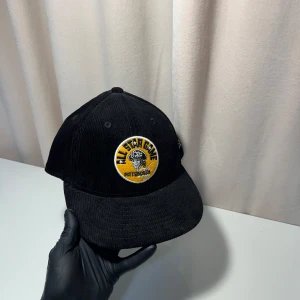 New Era keps - Snygg svart keps från New Era med broderad logga framtill och på sidan. Kepsen har en klassisk design med rundad skärm och är tillverkad i manchestertyg. Perfekt för en stilren look.
