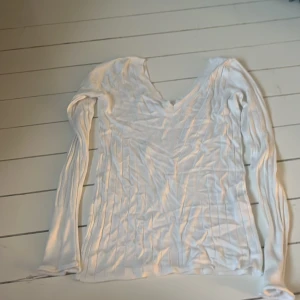 Vit ribbad tröja - Säljer en stilren vit ribbad tröja med långärmad design. Tröjan har en v-ringad hals och är perfekt för en avslappnad look. Den är gjord i ett mjukt material som känns skönt mot huden.
