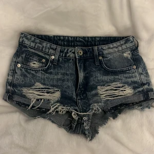 Lådmidjade jeansshorts - Säljer ett par coola blå jeansshorts från H&M med slitna detaljer och låg midja. De har en rå kant nertill som ger en extra edge. Midjemått tvärsöver: 34-35 cm. Säljer då de är för små för mig 💕