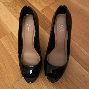 Svarta pumps med öppen tå - Eleganta svarta pumps med öppen tå och hög klack. Skorna har en glansig finish som ger en stilren look. Perfekta för en utekväll eller ett speciellt event. Pris kan diskuteras✨