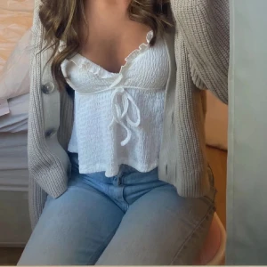 Vit topp från Shein - Säljer en söt vit topp från Shein med knytning framtill och volangdetaljer vid axlarna. Toppen är ärmlös och har en smickrande passform. Perfekt för varmare dagar eller som ett lager under en kofta. Köpt från plick (första bilden är tagen från den förra säljaren)