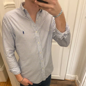 Rutig skjorta från Ralph Lauren - Säljer en stilren rutig skjorta från Ralph Lauren i blått och vitt. Skjortan har en slim fit passform och långa ärmar med knappar. Perfekt för en snygg och avslappnad look. Modellen är ca 182, tveka inte att kontakta vid eventuella frågor 😀