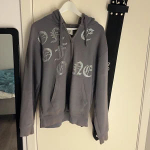 Grå One Of One hoodie - Säljer en grå one of one hoodie. Den har en klassisk design med huva och fickor. Perfekt för en avslappnad stil.