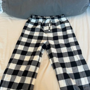 Svartvita rutiga pyjamas byxor - Snygga och bekväma byxor med svartvitt rutmönster. De har en elastisk midja med snörning för extra komfort. Perfekta för en avslappnad stil.