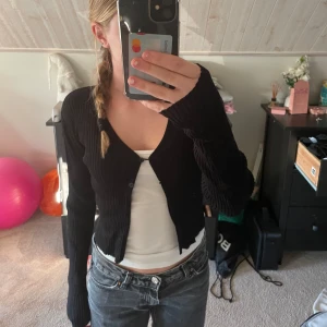 Svart ribbad kofta från Samsa Young - Säljer en stilren svart ribbad kofta från Samsa Young. Koftan har en v-ringning och knappar framtill. Den är croppad och har långa ärmar, perfekt för en trendig look. Passar bra till både jeans och kjol. Jättesöt och inte andvänd många gånger! Pris kan diskuteras💕