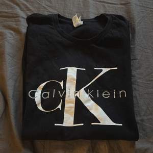 Säljer en svart t-shirt från Calvin Klein med stort vitt CK-logotyptryck på framsidan. Perfekt för en stilren och avslappnad look.