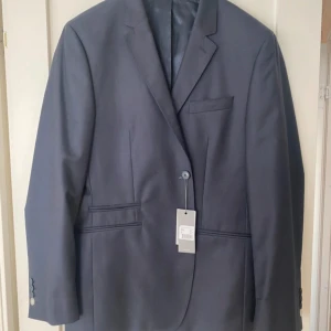 Mörkblå kavaj från Atlas design  - Elegant mörkblå kavaj med klassisk design. Kavajen har en enkelknäppt front och fyra knappar vid ärmsluten, varav en är ljusare. Perfekt för formella tillfällen.