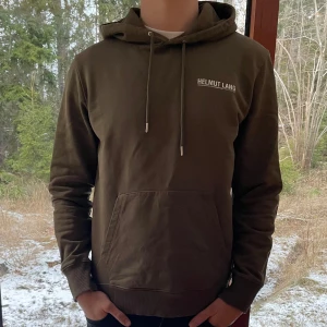 Olivgrön hoodie från Helmut Lang - Säljer en snygg olivgrön hoodie från Helmut Lang med tryck på bröstet. Skick 9/10 då den är sparsamt använd. Storlek L men passar även M. Pris kan diskuteras vid snabb affär.
