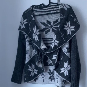 Grå kofta med snöflingemönster - Supergullig mysig kofta med vitt snöflingemönster. Den har långa ärmar och en knytning framtill. Väldigt mysig och kan lätt liva upp en basic outfit! Tveka inte på att ställa frågor eller lägga prisförslag😊