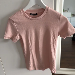 Rosa t-shirt från Zara - Säljer en söt rosa t-shirt från Zara. Den är kortärmad och gjord i mjuk bomull, perfekt för en avslappnad stil. Enkel och stilren design som passar till det mesta. 🌸