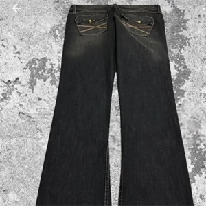 Svarta bootcut jeans - Väldigt lågmidja jeans snygga svarta bootcut jeans med slitna detaljer och fickor med knappar bak. 38midjan 73innerbenslängd och lårbredd21