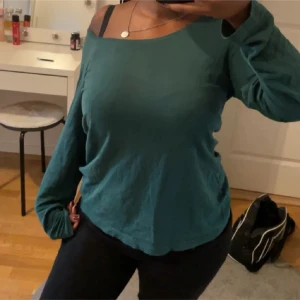 Grön långärmad topp - Säljer en stilren grön långärmad topp med en offshoulder-design. Perfekt för en avslappnad look. Toppen har en mjuk och bekväm passform.