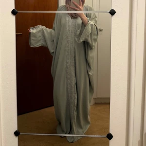 Ljusgrön abaya med broderade detaljer - Elegant ljusgrön Laila abaya med vackra broderade detaljer längs framsidan och ärmarna i silver och pärlor. Den har en lös passform och vida ärmar som ger en flytande och bekväm känsla. Perfekt för student mottagning, förlovning, fest etc. Köpt på Classybyy org pris 650kr (passar XS-XL) 142cm!