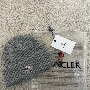 Moncler mössa - Säljer denna gråa mössa från Moncler. Den är i bra skick och är riktigt snygg. Passar för kalla dagar. Dustbagen ingår i köpet.