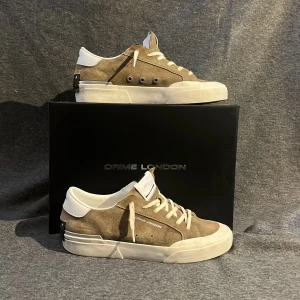 Bruna sneakers från Crime London - Snygga bruna sneakers från Crime London i mocka med vita detaljer och snörning. Skorna har en stilren design med en robust sula och diskreta logotyper. Perfekta för en avslappnad stil. Skick 10/10 ändast använda ett fåtal gånger. Stl/42 men passar även 43 